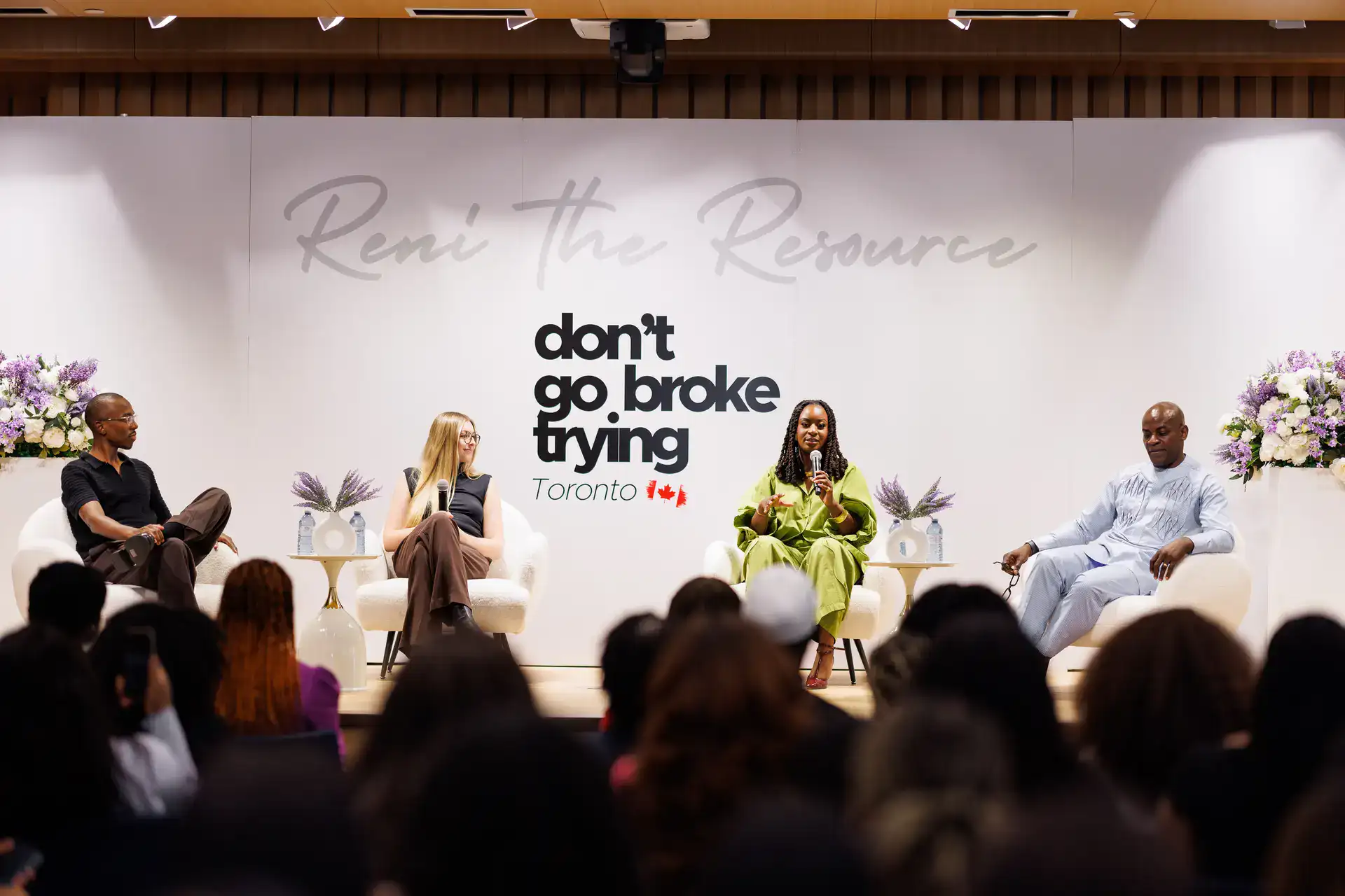 Four panelists in white armchairs on stage, one woman speaking into a microphone before an audience