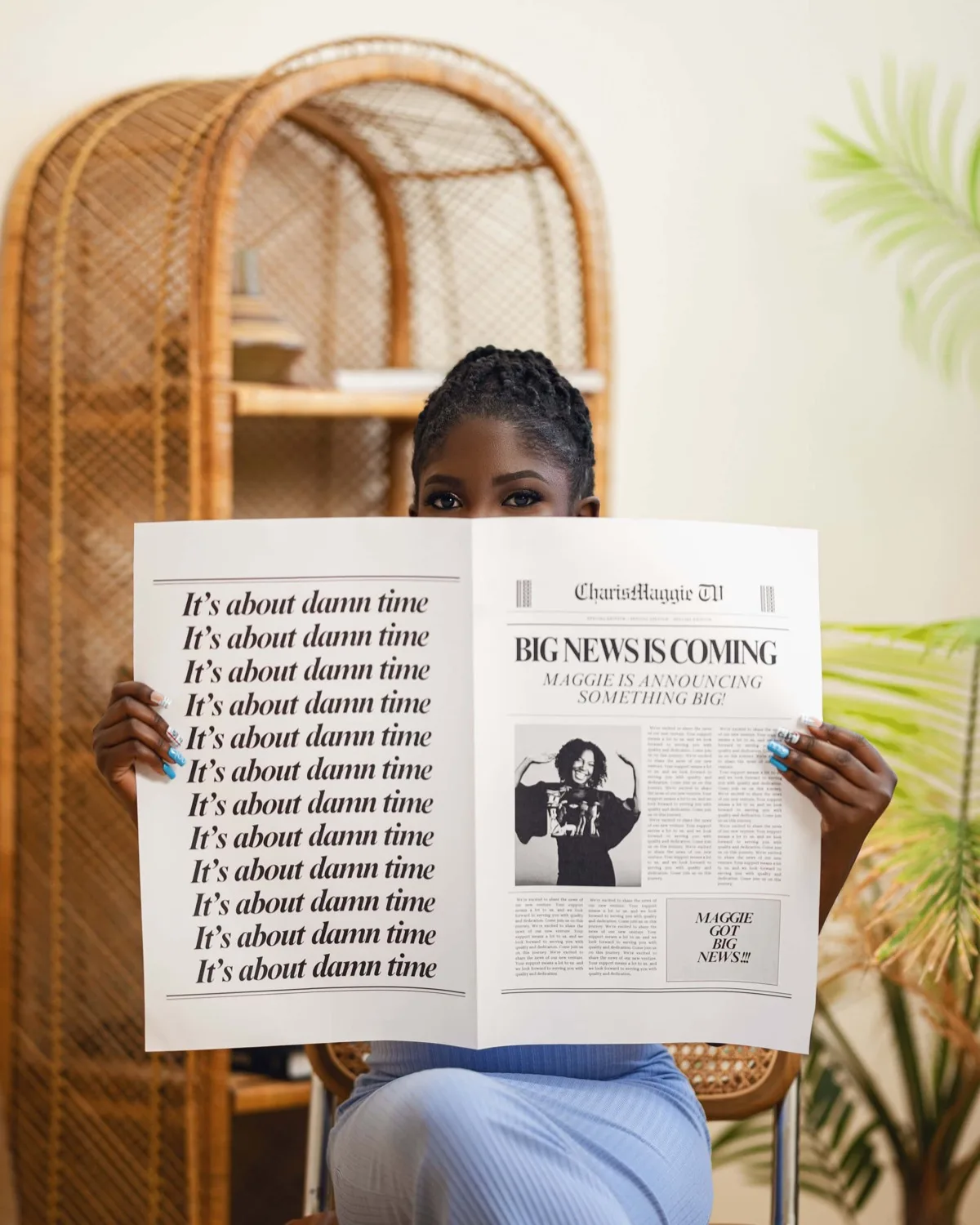 Woman holding mock newspaper announcing big news, covering face, seated by rattan chair and plants