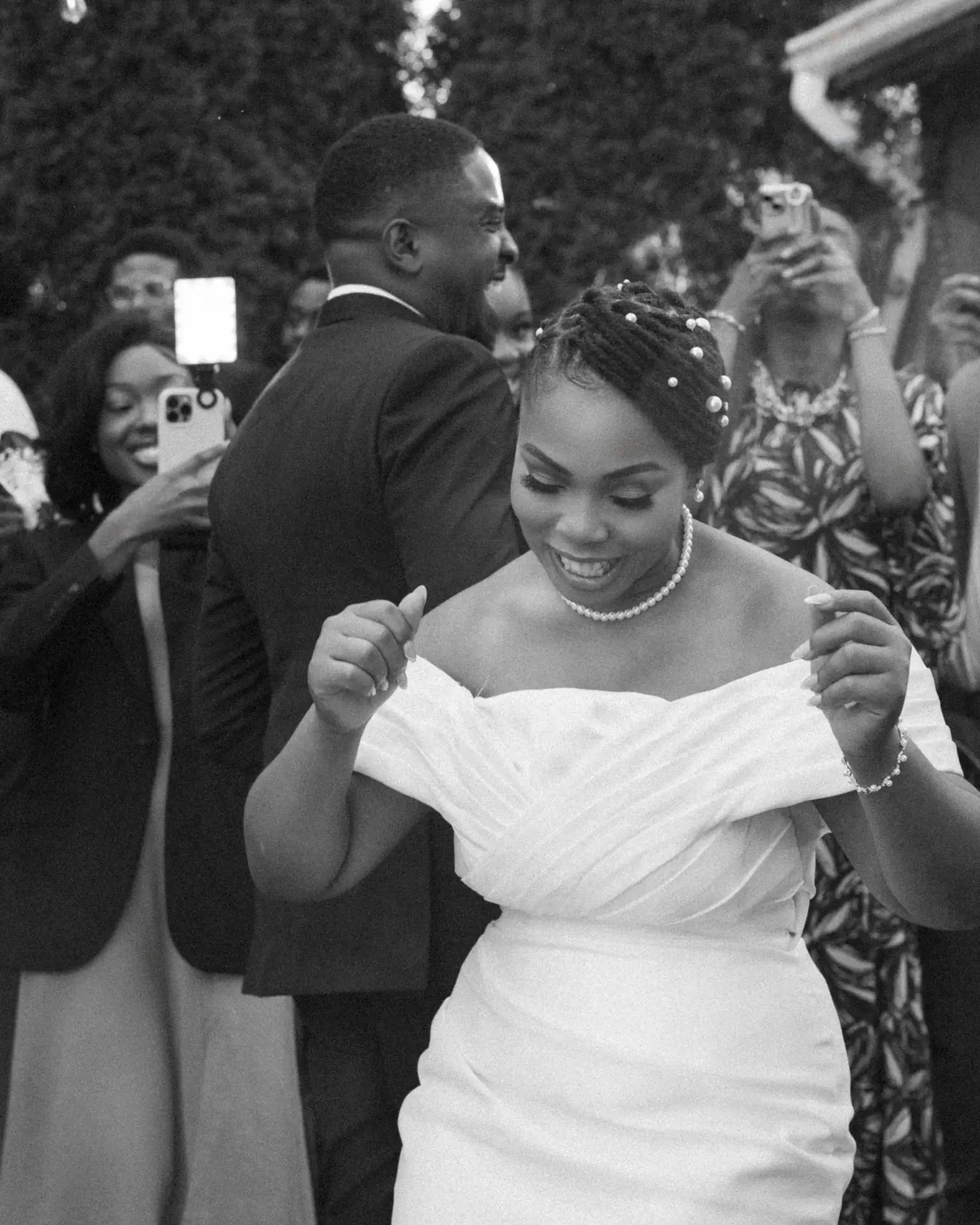 Bride with pearl-adorned hair dancing outdoors while guests record with their phones