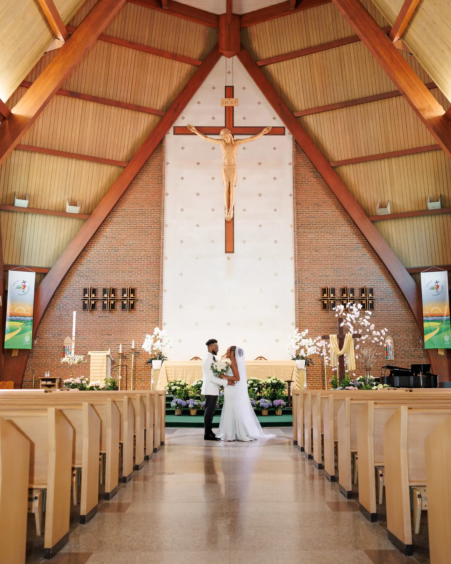 Bride and groom embracing at the altar of a soaring wooden church beneath a crucifix