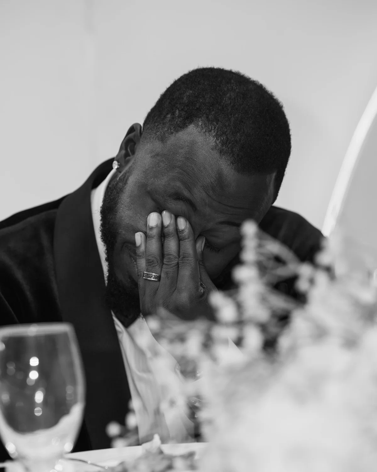 Groom seated at the reception table wiping away tears behind a floral centerpiece