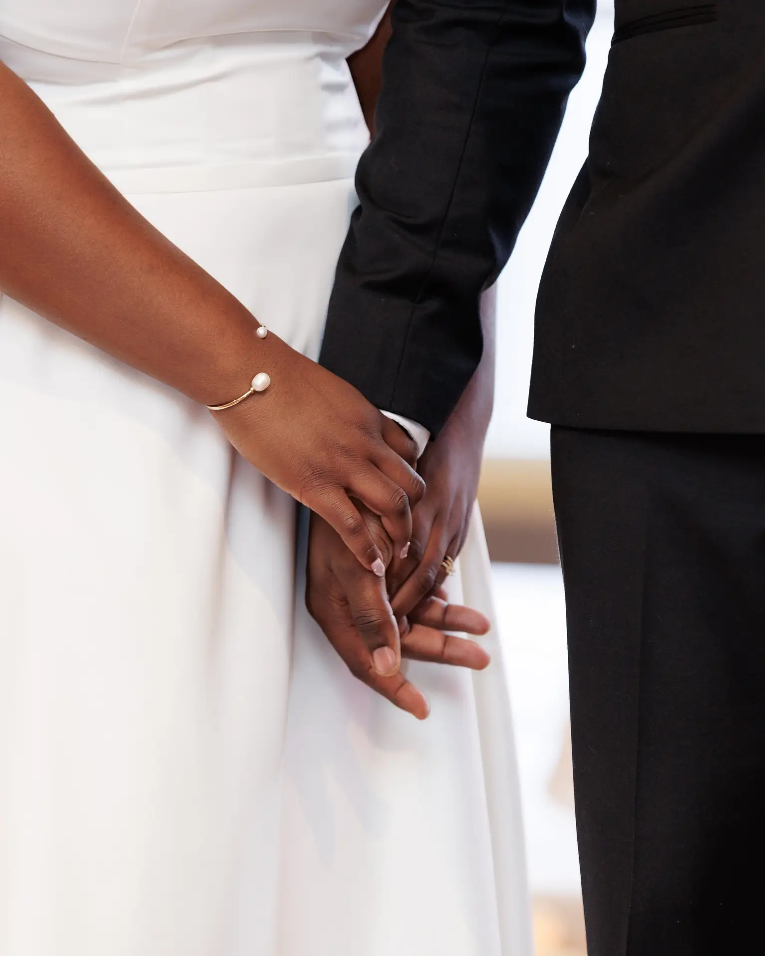 Close-up of bride and groom's intertwined hands against white gown and dark suit